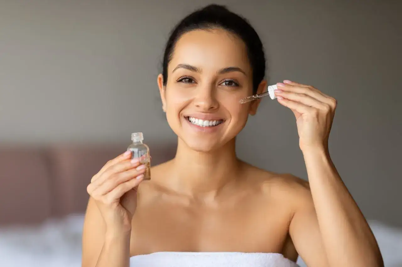 Uśmiechnięta kobieta aplikuje serum na twarz. W składzie kosmetyku może być hexyl cinnamal, który nadaje mu przyjemny zapach.