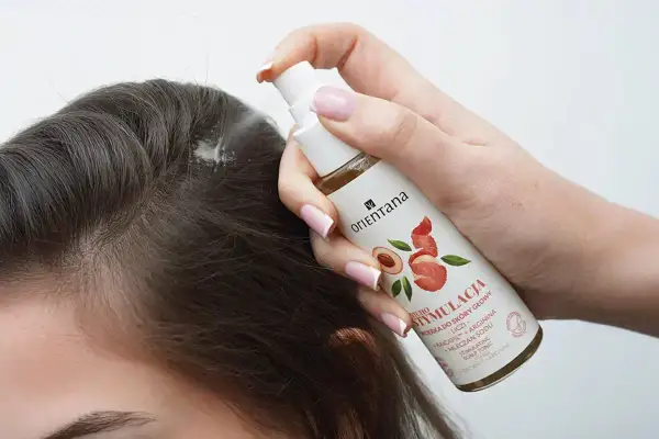 Dłoń aplikuje spray na skórę głowy, szukając odpowiedzi na pytanie: jakie witaminy na wypadanie włosów?