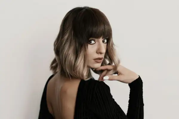 Kobieta z ciemnymi, ombre włosami w stylu blunt bob, z mocnym makijażem oczu, w czarnej, welurowej sukience.