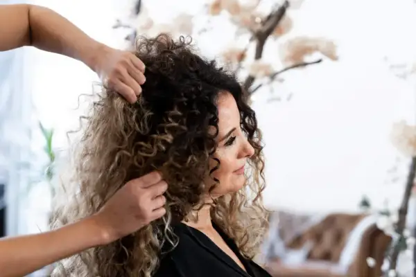 Stylista układa bujne, kręcone włosy kobiety, pokazując, jak obciąć kręcone włosy, by podkreślić ich naturalny skręt.